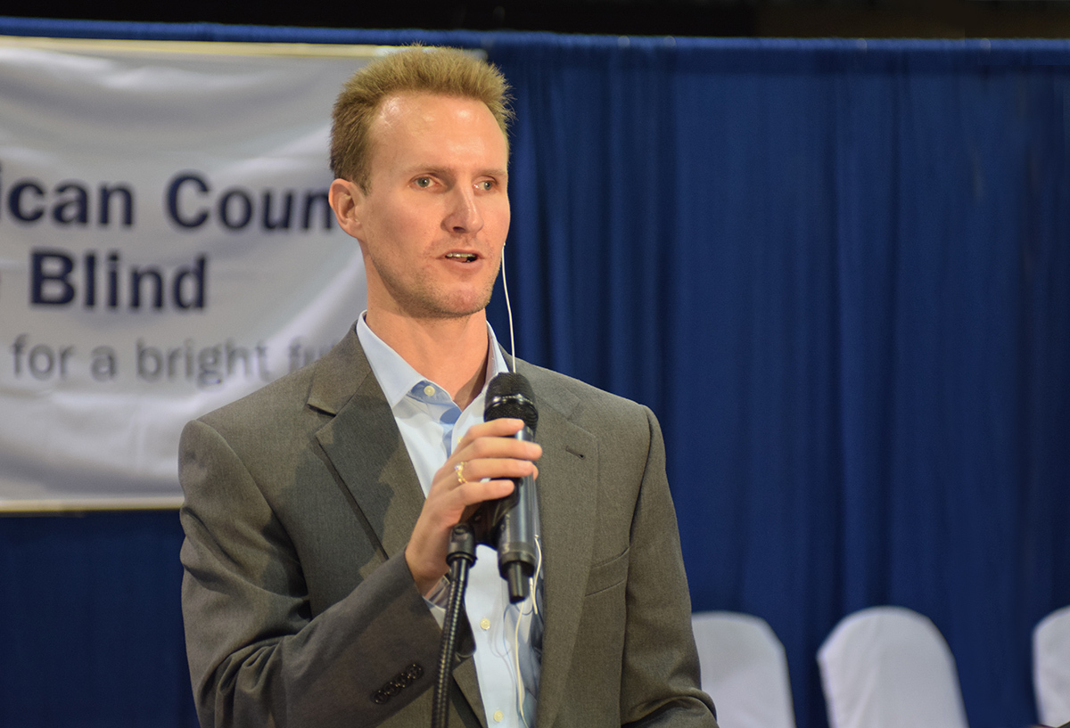 Clark Rachfal, director of advocacy and governmental affairs, talks in depth about ACB’s legislative imperatives. He stands on stage at the front of the room, holding a portable microphone.