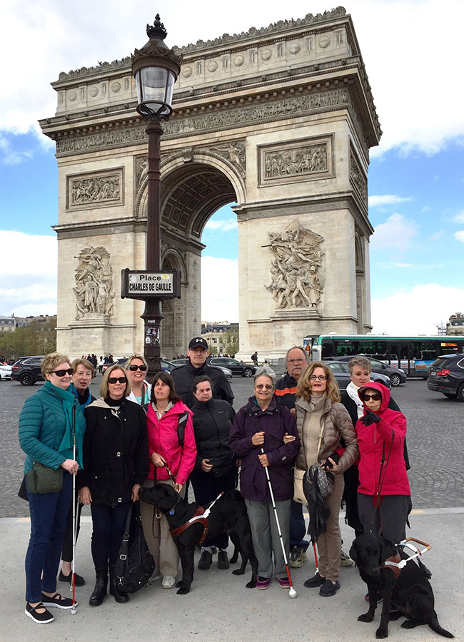The travel group in front of the Arc de Triomphe in Paris. Katie Frederick, third from left, sports a hot pink jacket and is holding onto her guide dog's harness. Vicky Prahin stands next to Katie wearing a black jacket.