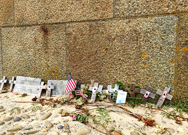 Wooden crosses, American flags, and seashells lay among the graves of American soldiers buried in Normandy.
