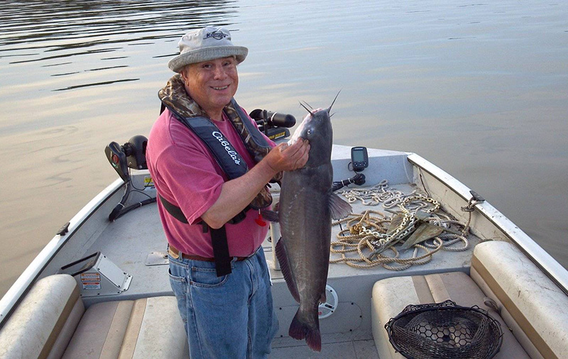 Ron Milliman examines the catfish he’s just reeled into the boat. He carefully avoids the sharp “whiskers” on the fish’s face.