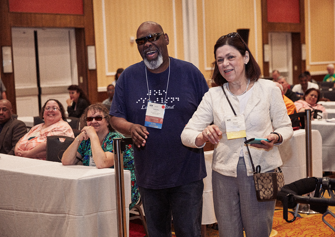An ACB employee guides a smiling ACB member to the podium during a meeting